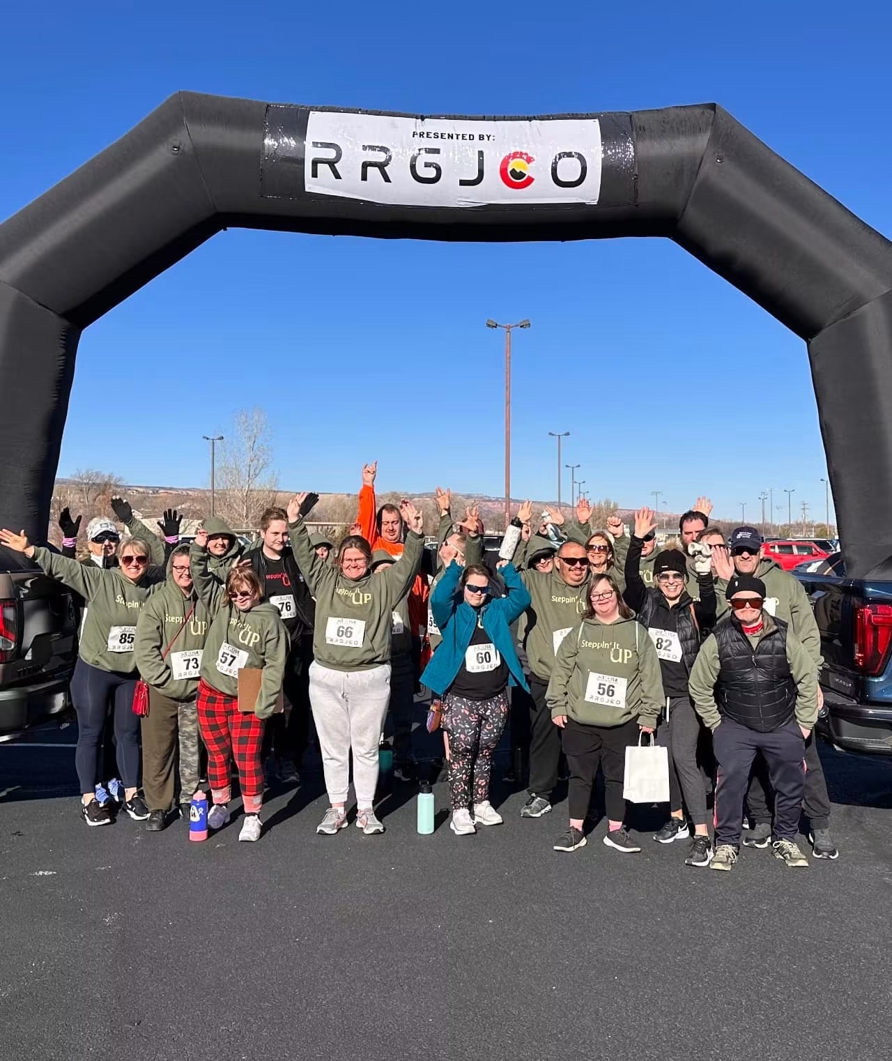 Athletes with race bibs cheering under a start line arch