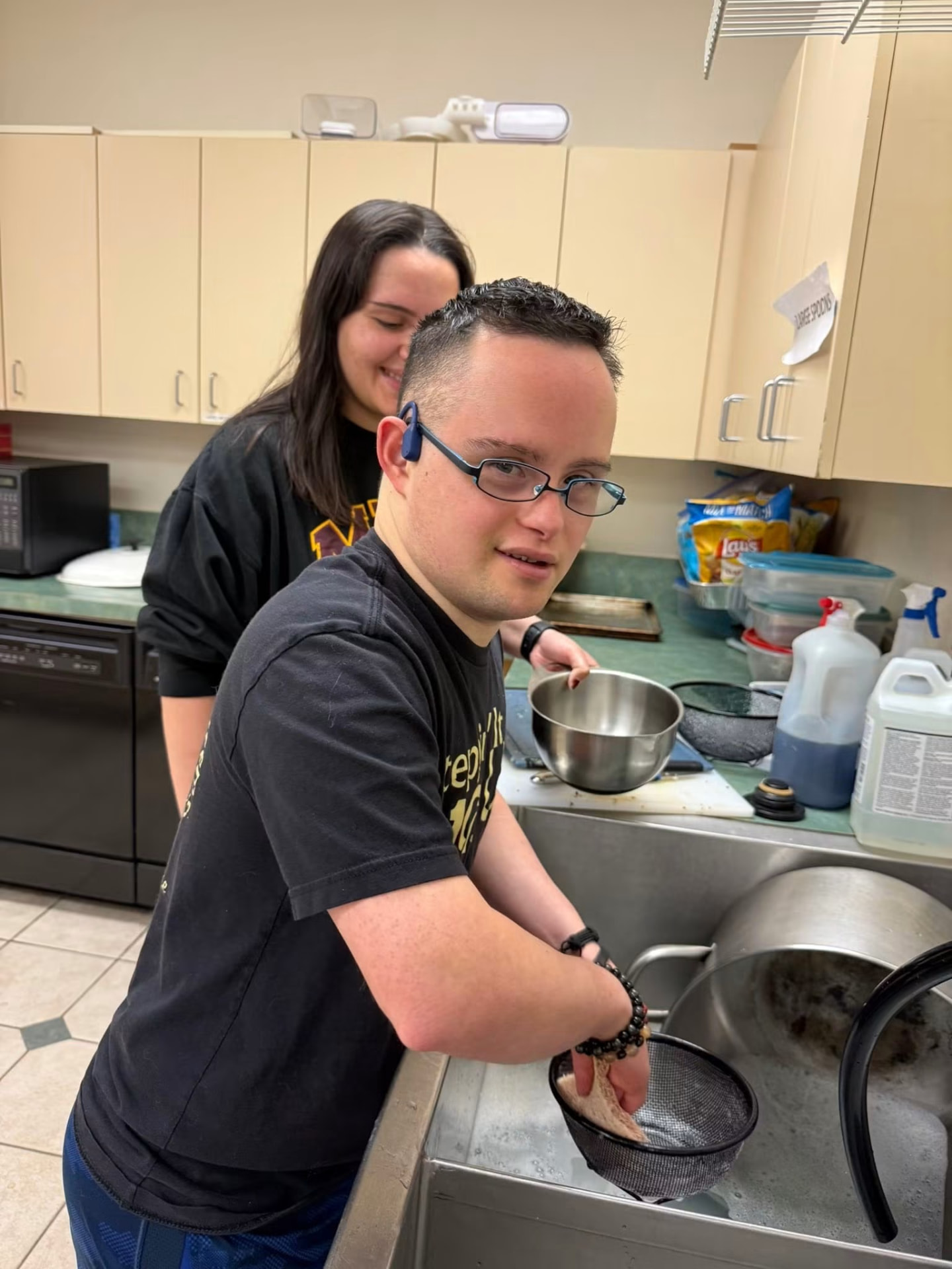 Athlete washing dishes in the kitchen with a helper nearby