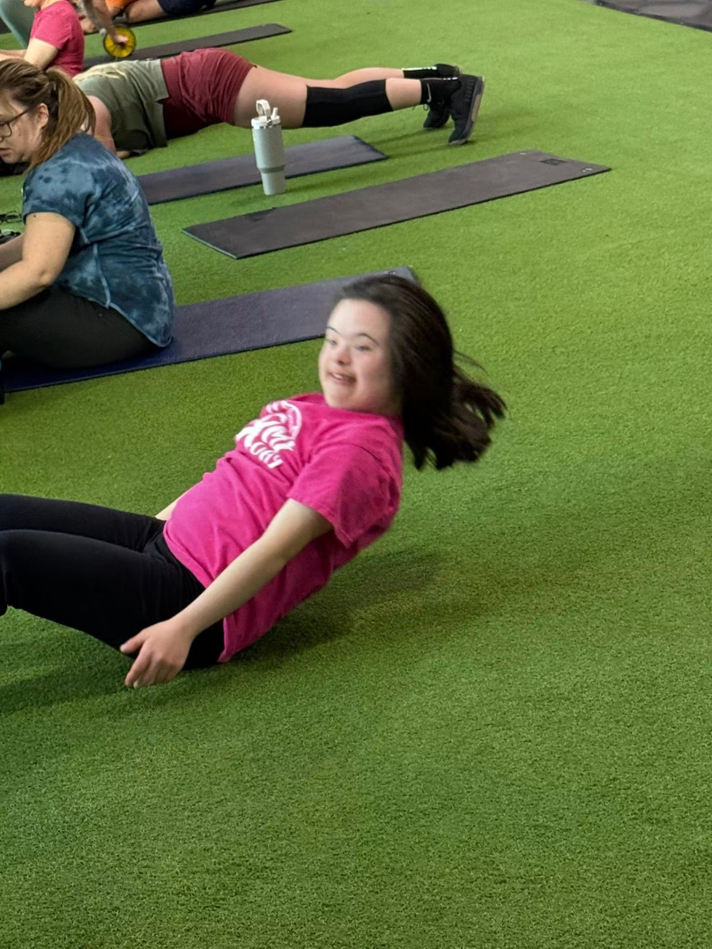 Athlete in a pink Steppin' It Up shirt smiling during core work on the turf